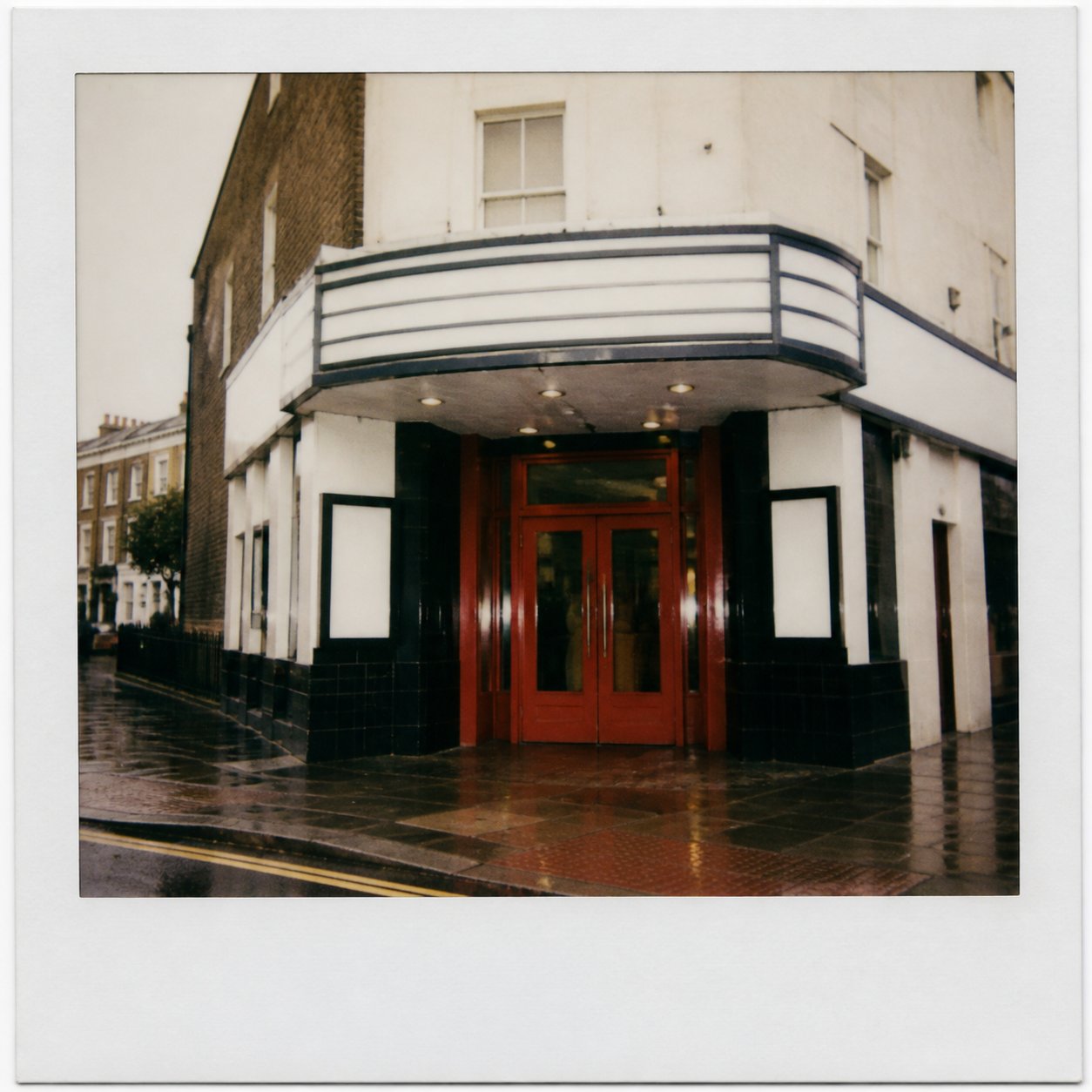 A wet Soho street at night, the glow of a small cinema entrance.